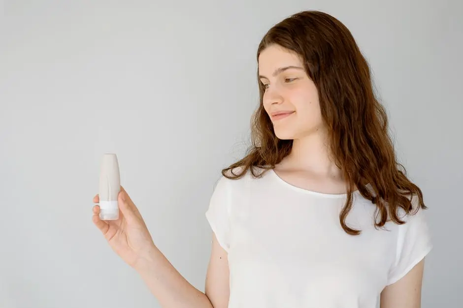 alt wanita muda di kamar sederhana tersenyum sambil memegang botol skincare lokal